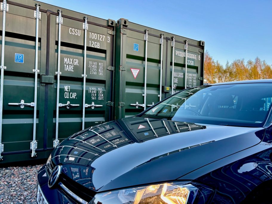 a motor car parked next to two shipping containers