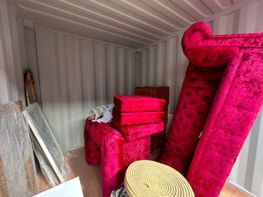 Vibrant pink furniture, including upholstered chairs and cushions, arranged in a shipping container.