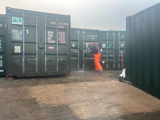 Worker in orange overalls cleaning the outside of storage containers on a self storage facility.