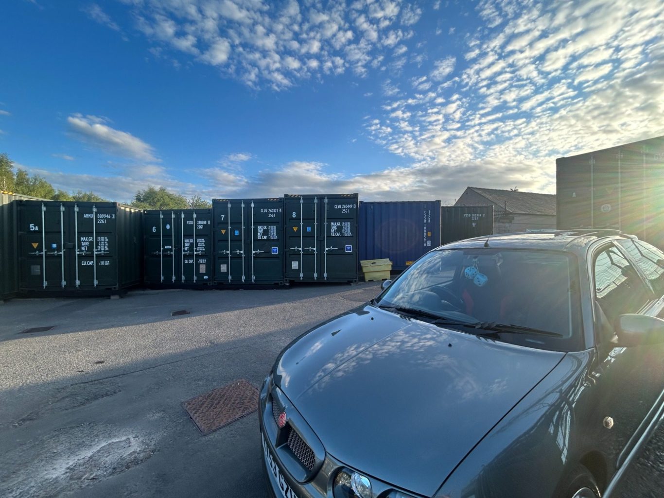 silver car parked infront of shipping containers with a large turning circle highlighting the ease of turning on a self storage site.