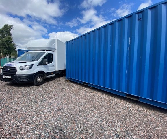 A white van parked next to a large blue shipping container.