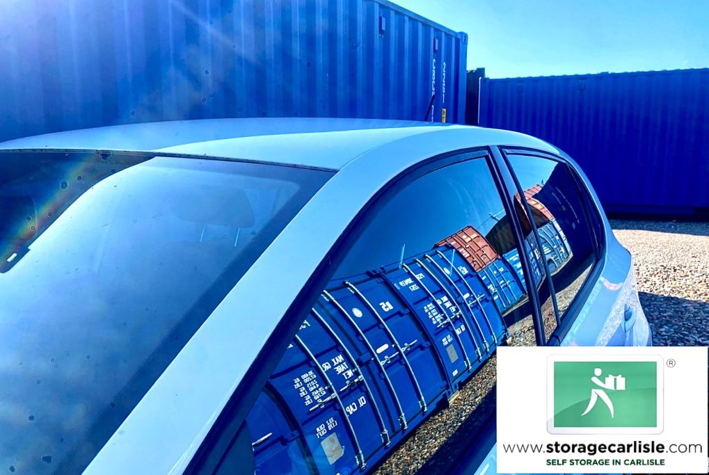 a car parked on a storage facility next to a row of shipping containers